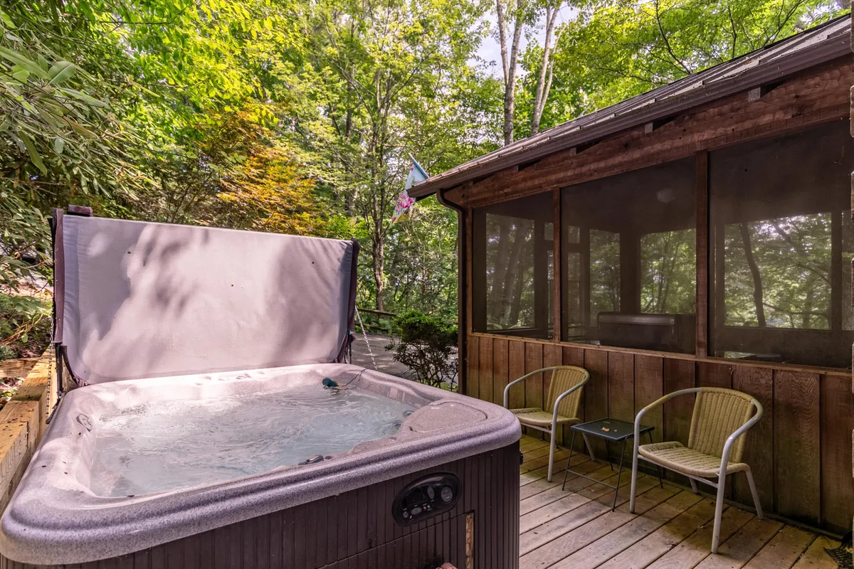 This image showcases a hot tub situated on a screened porch surrounded by lush greenery. The inviting outdoor setting hints at opportunities for stargazing at night or enjoying a soothing soak while immersed in nature. The comfortable seating and tranquil ambiance create the perfect environment for relaxation and romance.