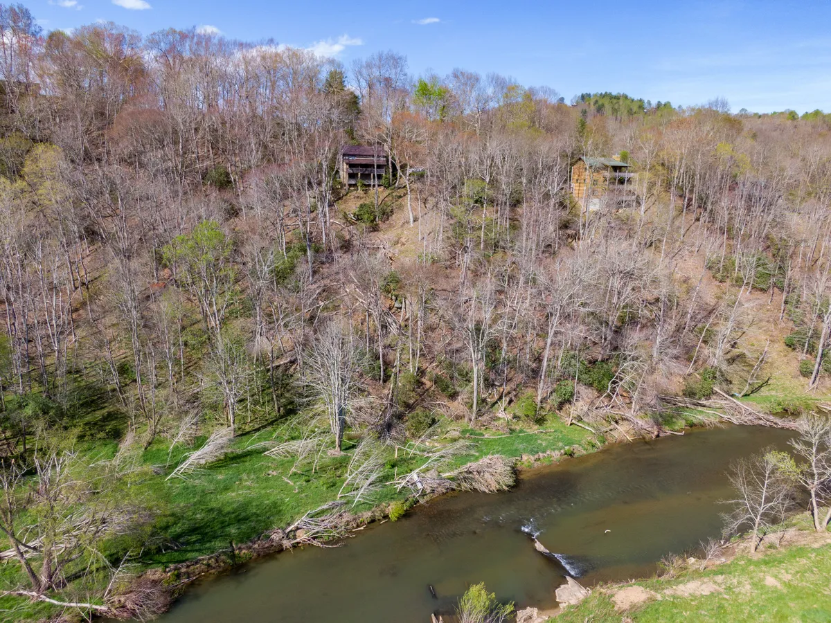 This image features a tranquil river winding through a lush landscape, framed by trees and distant hills. Houses can be seen perched on the hillside, suggesting proximity to local homes and amenities. The scene evokes a sense of peace, natural beauty, and the allure of outdoor adventure.