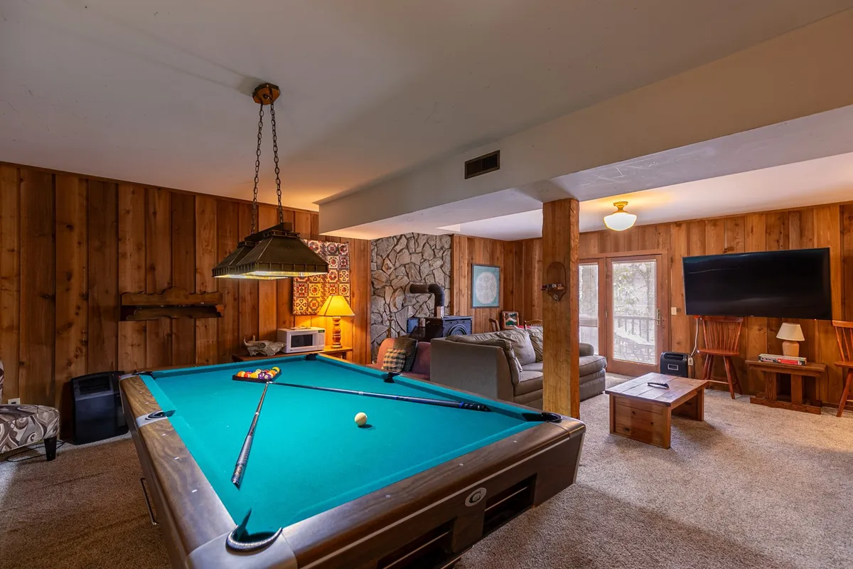 A cozy interior recreation room featuring a pool table, stone accent wall, comfortable seating area, and a TV. The space is designed for playing games, watching movies, or relaxing with friends and family.