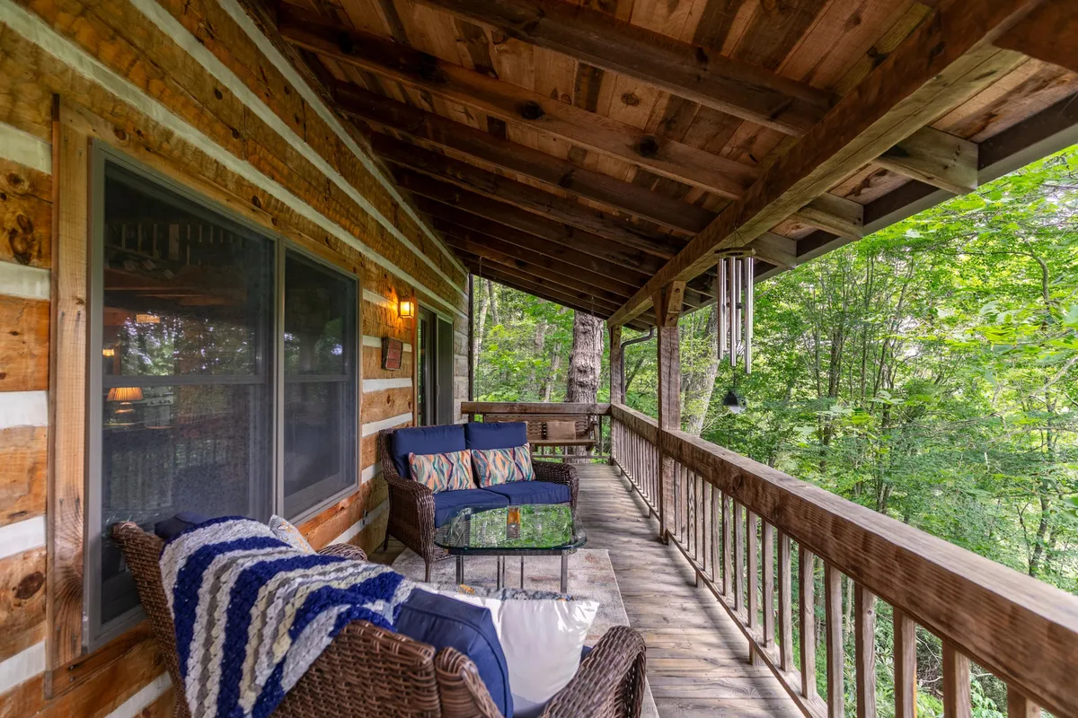 A comfortable outdoor seating area framed by a wooden railing, overlooking lush greenery. The inviting deck is perfect for sipping morning coffee, relaxing with a book, or simply enjoying the sights and sounds of the surrounding woods.