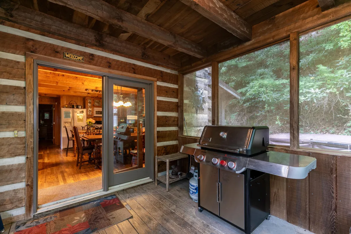 A welcoming exterior shot showing a grill beside an entrance door, with a dining area visible just inside. The setting hints at easy transitions between indoor and outdoor dining and a space well-suited for barbecues and gatherings.