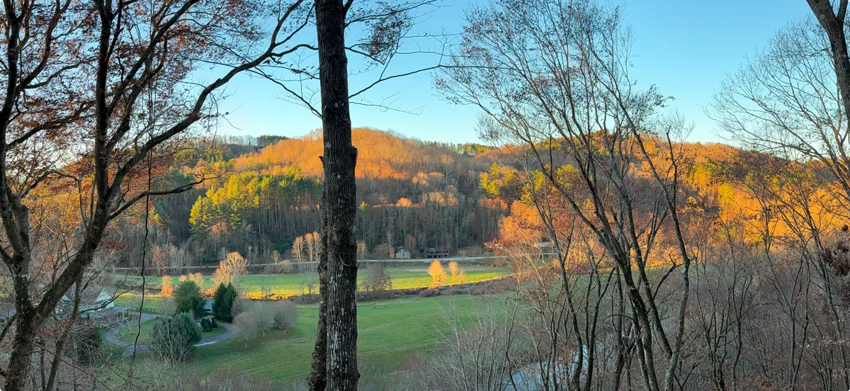 A broad scenic vista of rolling hills, a flowing river, and a backdrop of trees—ideal for hiking, bird watching, and picnicking. The mood is tranquil, with golden light suggesting either early morning or sunset, inviting families to explore, observe local wildlife, and enjoy the mountain air.