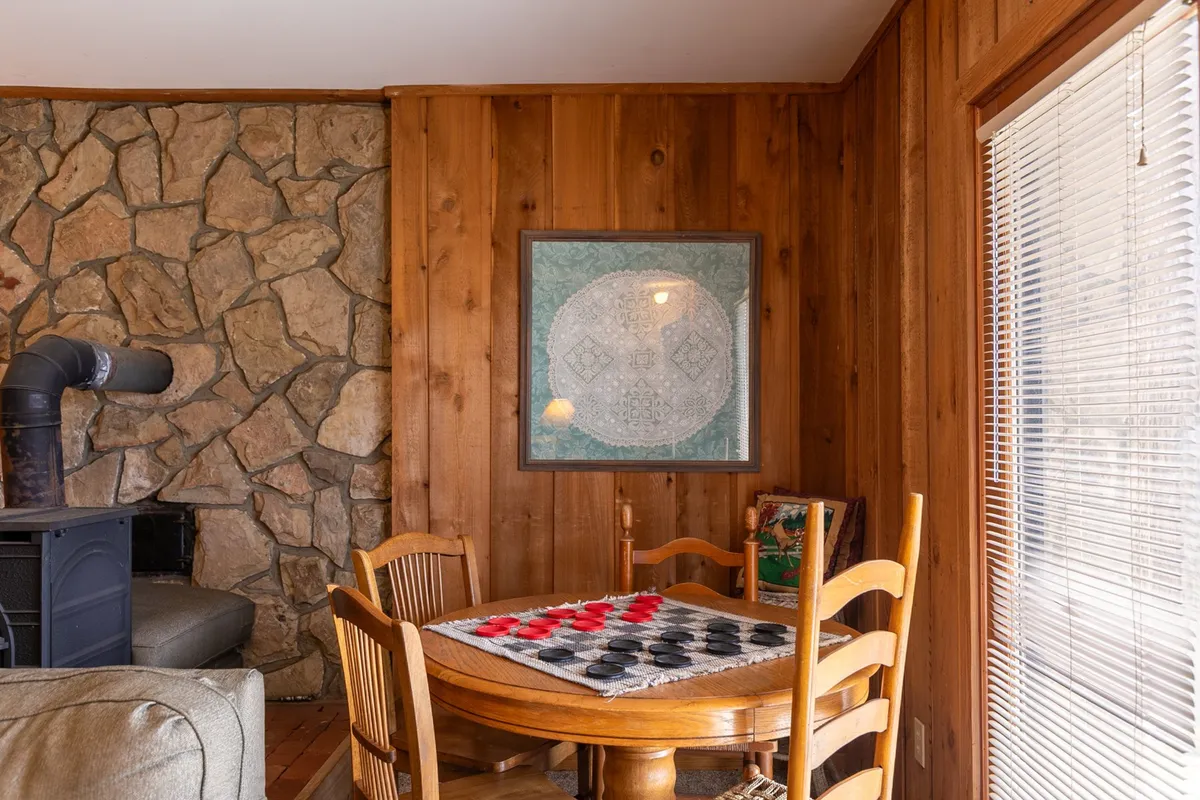 This image focuses on a wooden dining table set up with game pieces, a stone wall, framed artwork, and wooden chairs. It evokes the feeling of an inviting setting for board games, checkers, or puzzles, matching the description of family-friendly activities in the recreation room.