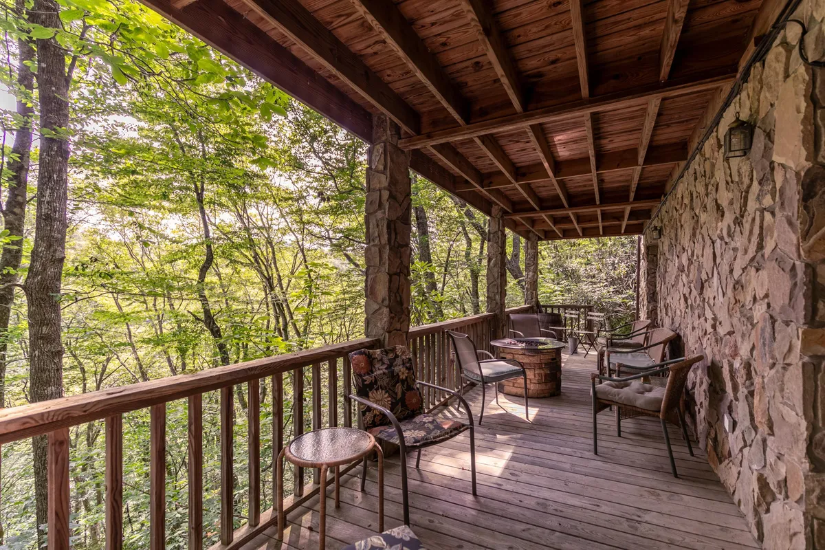 A peaceful outdoor seating area on a wooden deck with a stone wall and views of natural greenery. The arrangement includes comfortable chairs and a railing, suggesting a cozy spot to relax after outdoor adventures. The setting is tranquil, connecting indoor comfort with the surrounding nature.