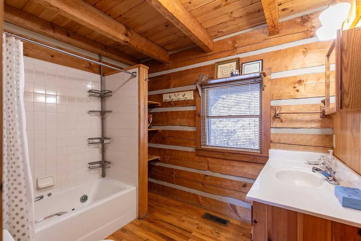 A warm and inviting bathroom with a deep bathtub surrounded by wooden beams and a nearby window, filled with soft lighting that creates a spa-like ambience. The space is perfect for relaxation, personal grooming, and unwinding after a day of adventure.