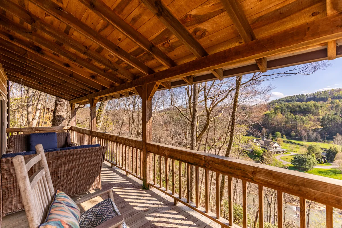 A deck scene with wooden railings and classic rocking chairs overlooking a scenic expanse of trees and hills. The setup invites guests to relax while taking in panoramic mountain and river views.