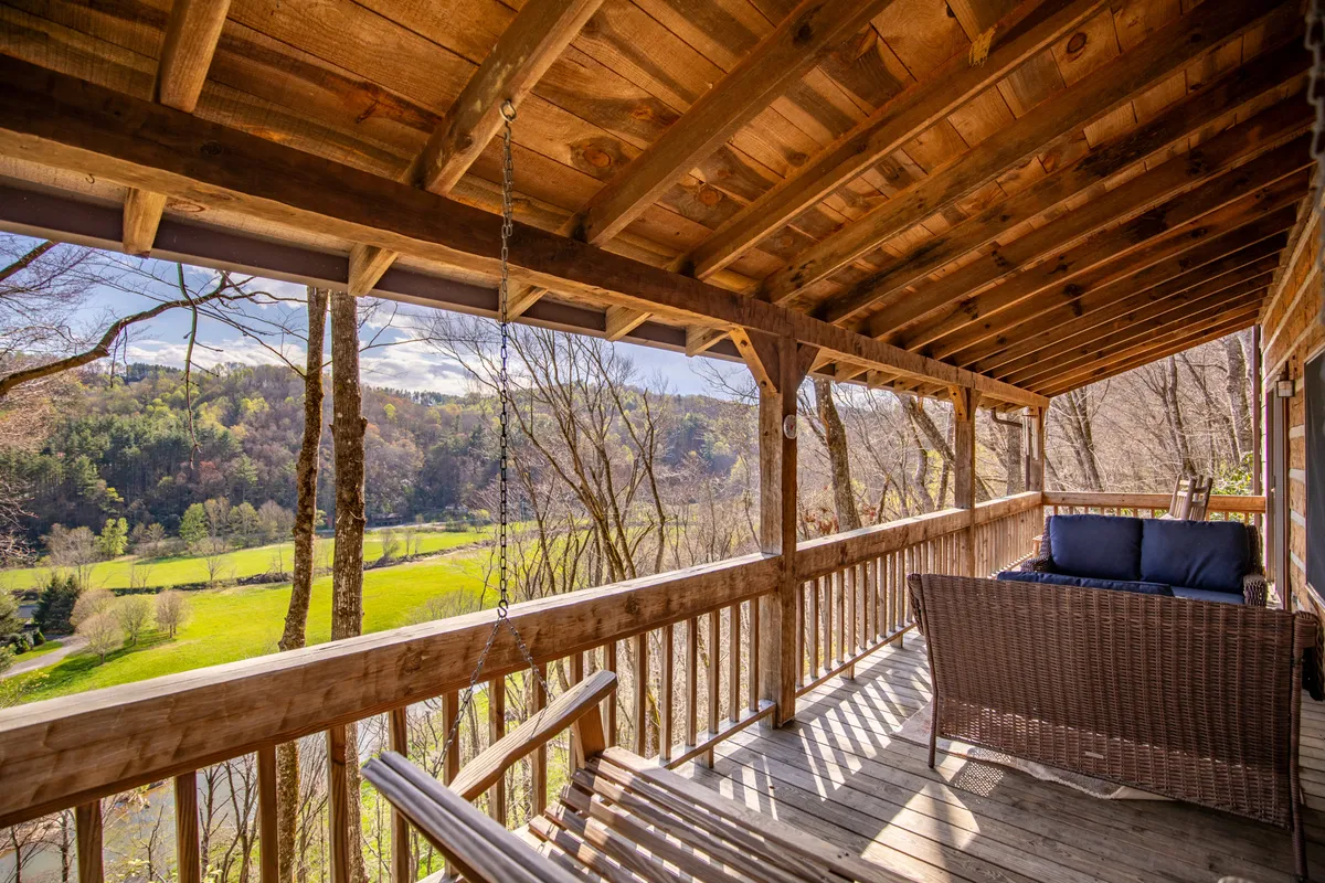 A tranquil exterior shot featuring a wooden structure with a swing and a seating area, surrounded by lush greenery. The swing and seating are positioned to take in scenic views, offering a peaceful spot for relaxation.