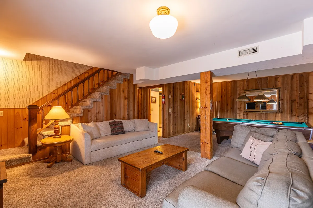 An inviting rec room featuring a comfortable sofa, coffee table, and a pool table at center stage. The space is ideal for socializing, playing games, and relaxing indoors after an active day.