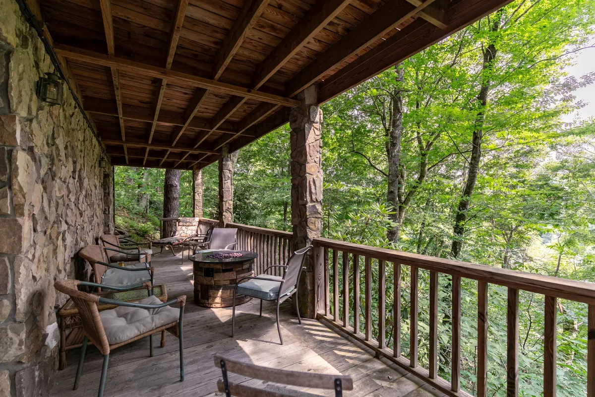 An outdoor seating area with wooden railings, stone walls, comfortable chairs, and a fire pit, set against a peaceful natural backdrop. The space is ideal for gatherings, socializing, and enjoying nature from sunrise to stargazing at night.