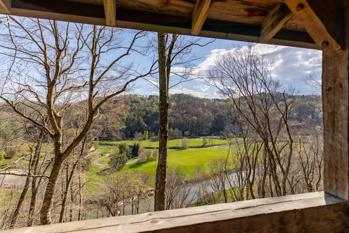 A sweeping view of lush green fields, a meandering river, bare trees, and distant hills. The natural landscape exudes tranquility and offers a direct connection to the river, mountains, and changing seasons mentioned in the section content.