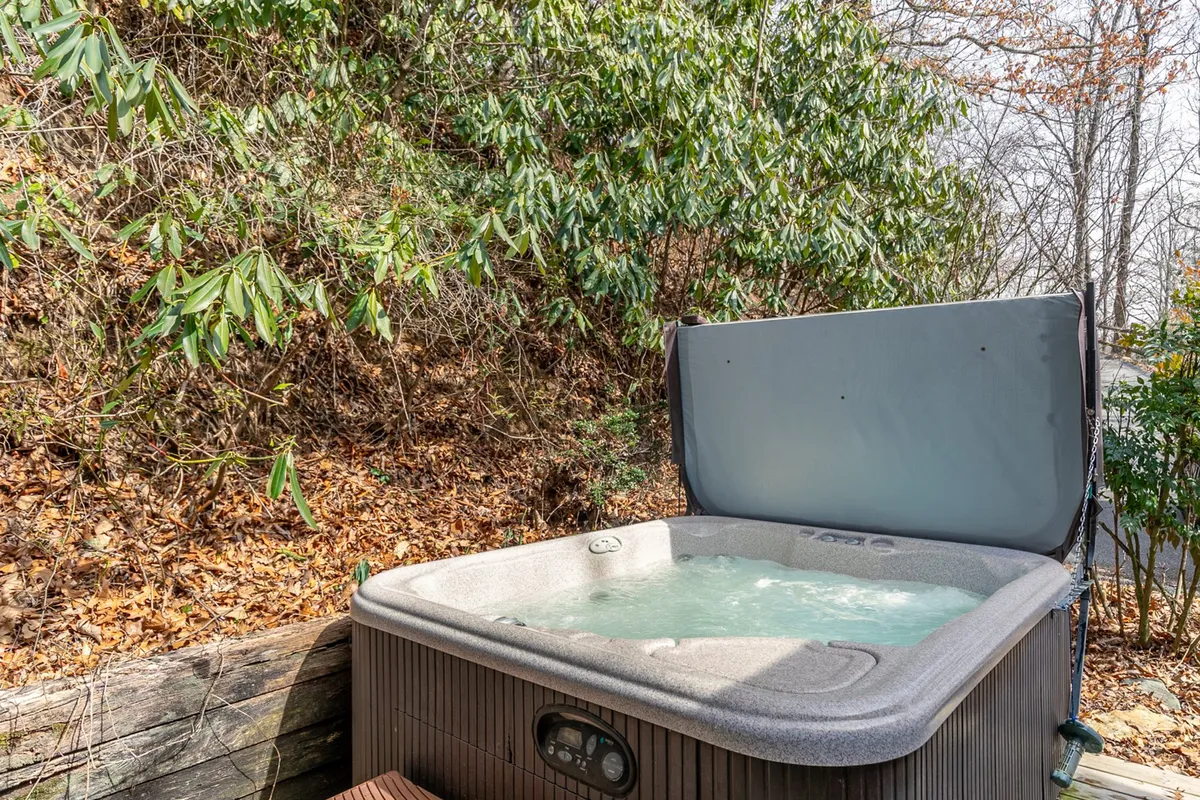 This image features a spacious hot tub nestled against a wooden structure, surrounded by lush greenery. The setting is tranquil, inviting guests to unwind and enjoy the serenity of the outdoors. Ample space and the natural backdrop highlight the relaxation possibilities after an adventurous day.
