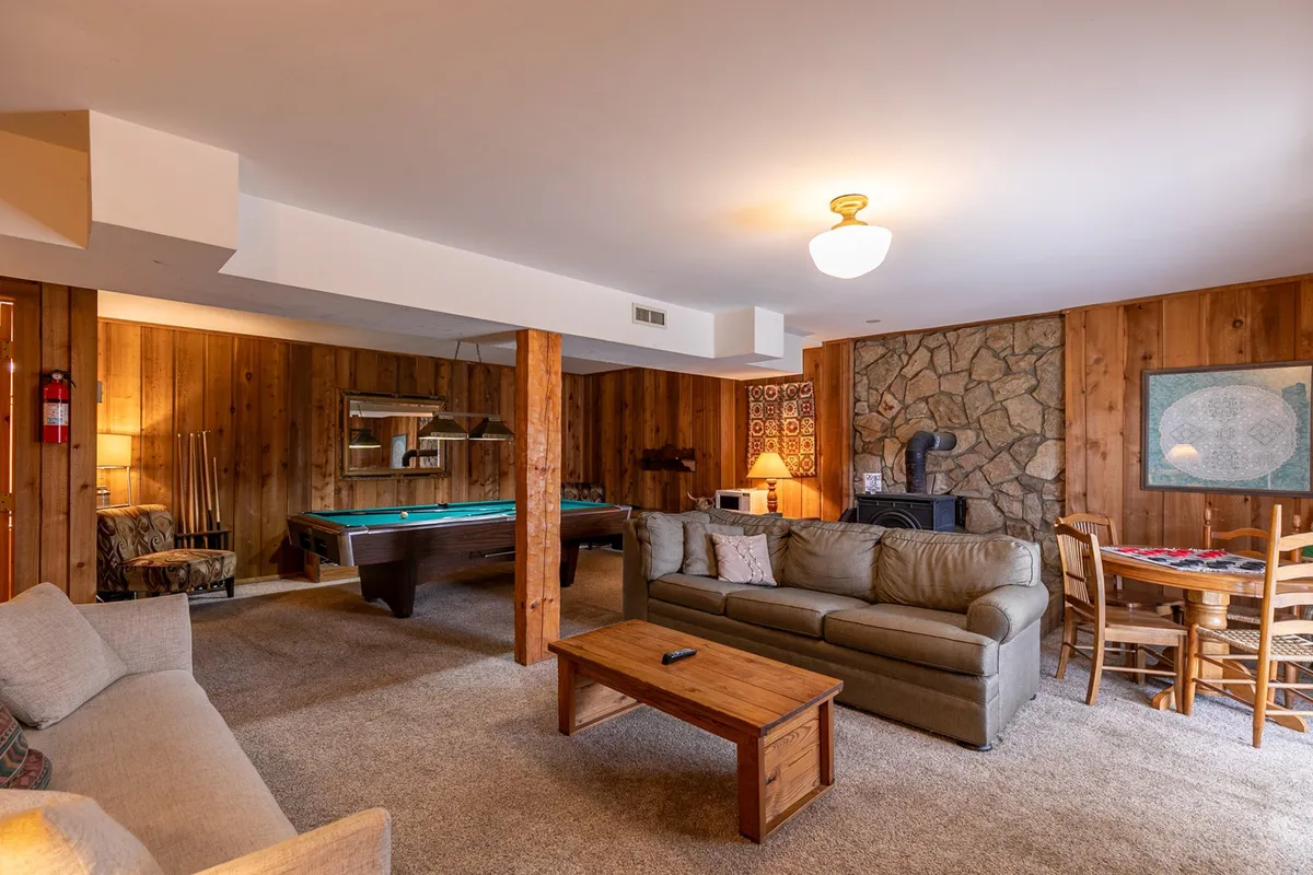 A spacious, comfortable recreation room featuring a pool table, fireplace, sofa, and dining table. The setting is designed for both relaxation and socializing, making it an ideal spot for game nights or unwinding after adventures. This space can also house the sleeper sofa for added private sleeping arrangements.